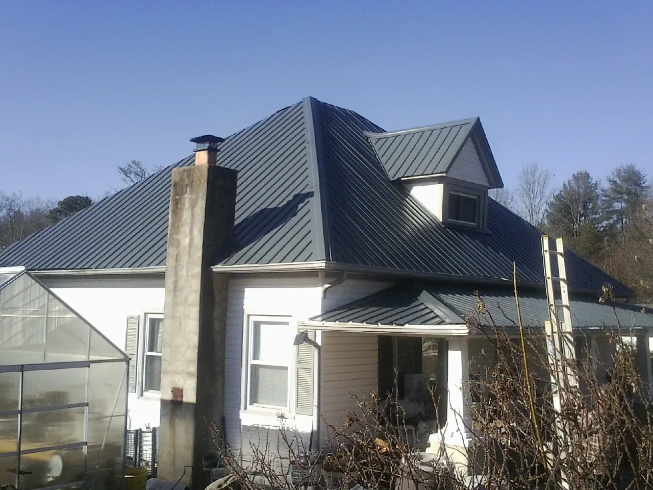 Dark blue standing seam metal roof on a white farmhouse with dormer — Slate & Tile Roof Repair by Roofing Brothers in Scarsdale