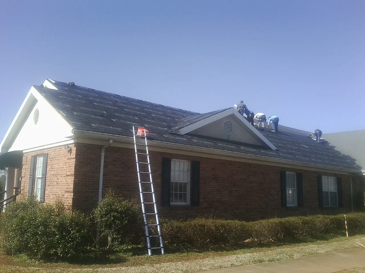Crew tearing shingles off a brick ranch roof with a ladder set — Emergency Roof Repair work by our crew in Scarsdale