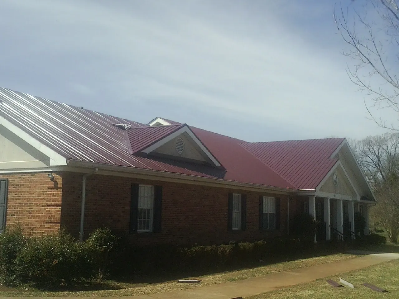 Red metal roof with gabled entries on a long brick building, from a Hail Damage Roof Repair job in Scarsdale