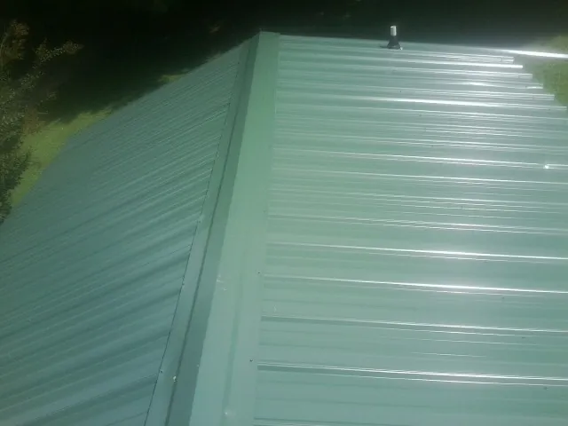 New green metal panels meeting at the ridge of a roof — Flat Roof Repair work by our crew in Scarsdale