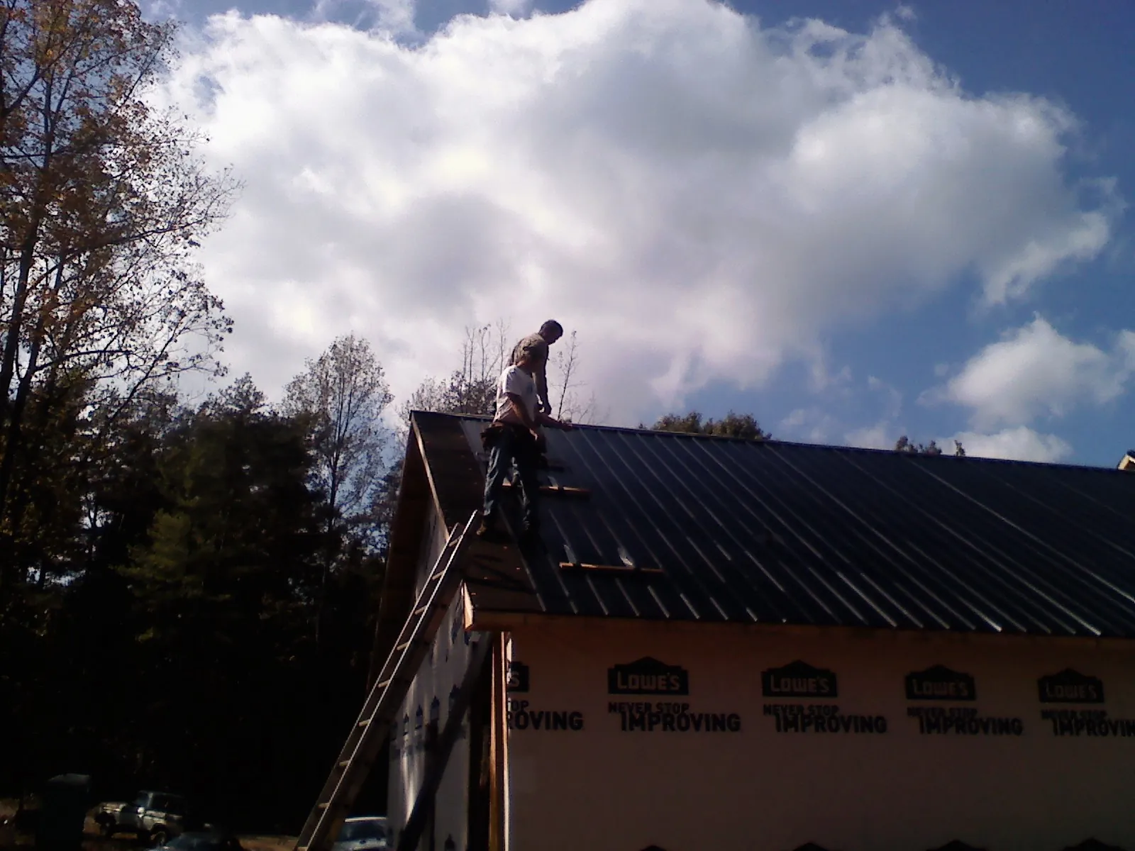 Roofer fastening dark metal panels high against a cloudy sky, from a Roof Inspection job in Scarsdale