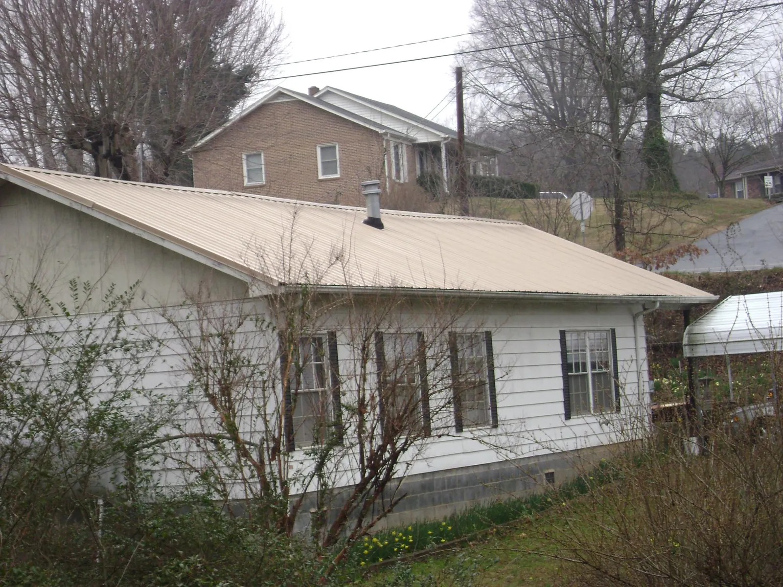 Tan metal roof on a white sided house set into a hillside — Commercial Roofing by Roofing Brothers in Scarsdale