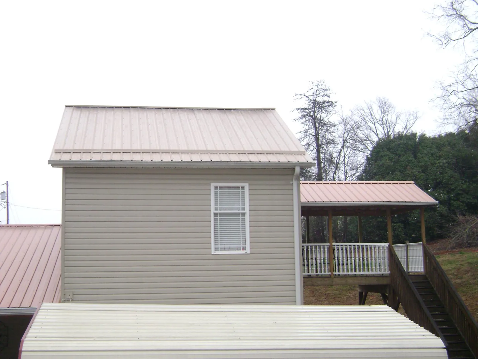 Tan metal roofs on a two story addition and attached porch, from a Roof Replacement job in Scarsdale